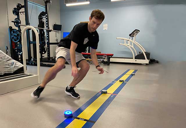 Patient using reactive agility training technology, dodging back and forth between lights on the floor.