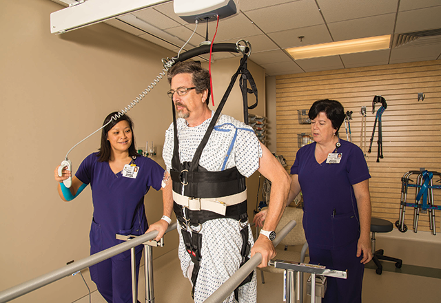 two therapists help a patient walk with the help of an overhead lift system