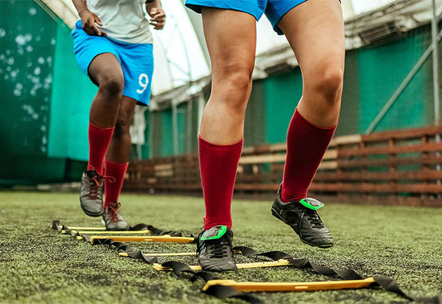 Two soccer players warming up before a game using rope ladder laid out on the field.