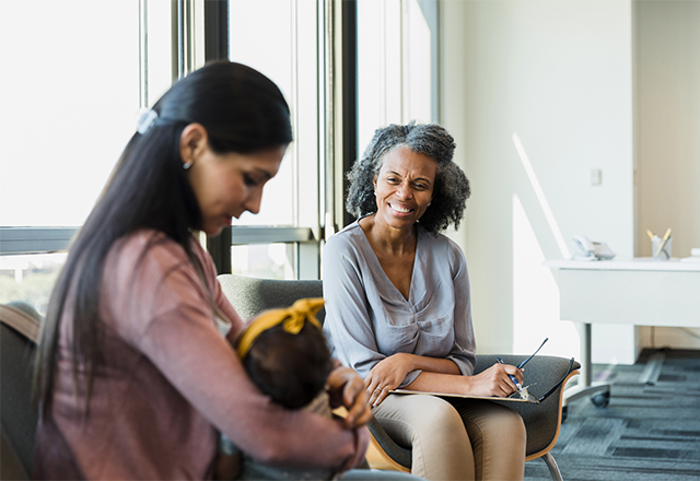 Mature female therapist smiles while watching mother interact with baby