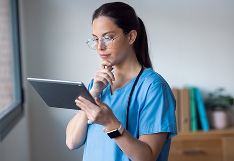 Female in medical scrubs looking at her digital tablet while standing