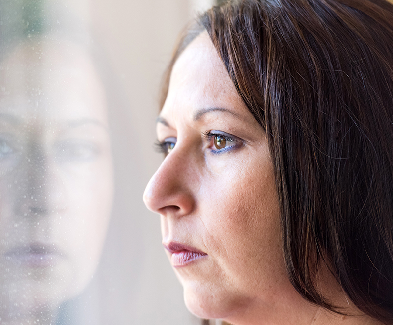 A woman looks out the window with a worried expression.