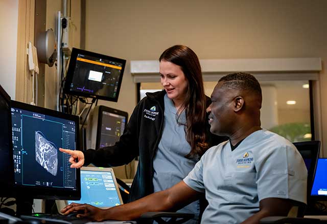 Two MRI techs, Joseph and Nikki, looking at a computer screen. Nikki is pointing at the MRI image on the screen.