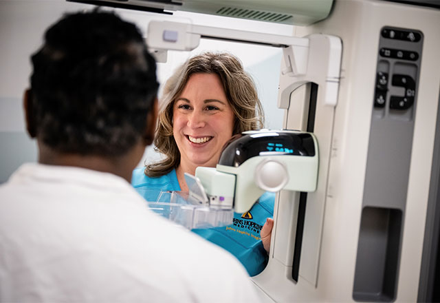 Radiologist and a patient standing in front of a mammogram machine.