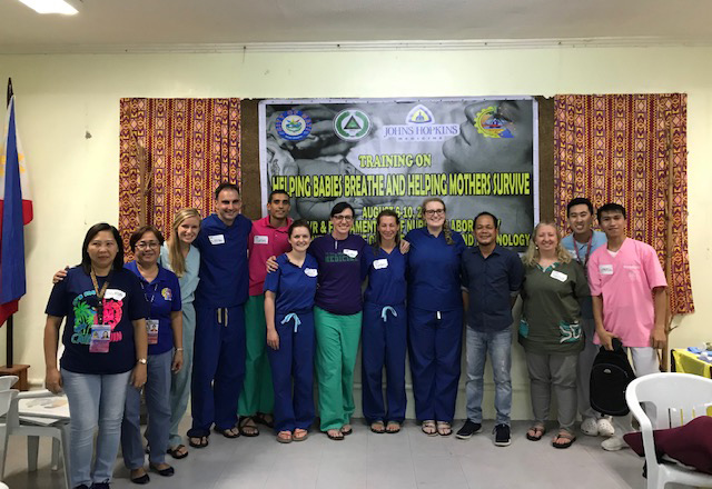 global health residents posing in front of maternal health poster