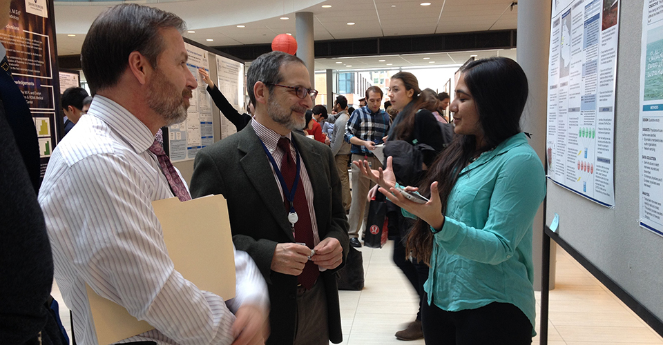 Researchers have a discussion in front of a research poster.