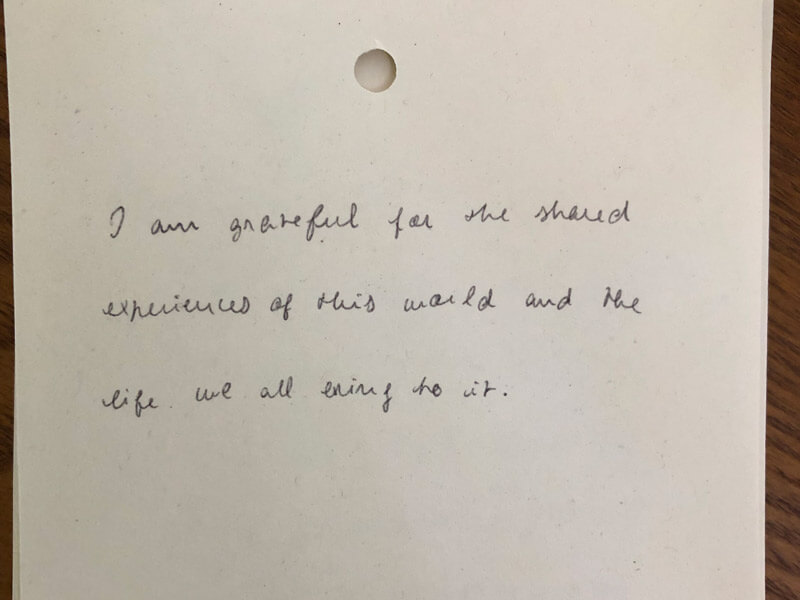 White note with cursive writing that reads "I am grateful for the shared experiences of this world and the life we all bring to it."