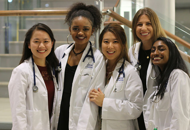 Students pose together wearing their white coats.