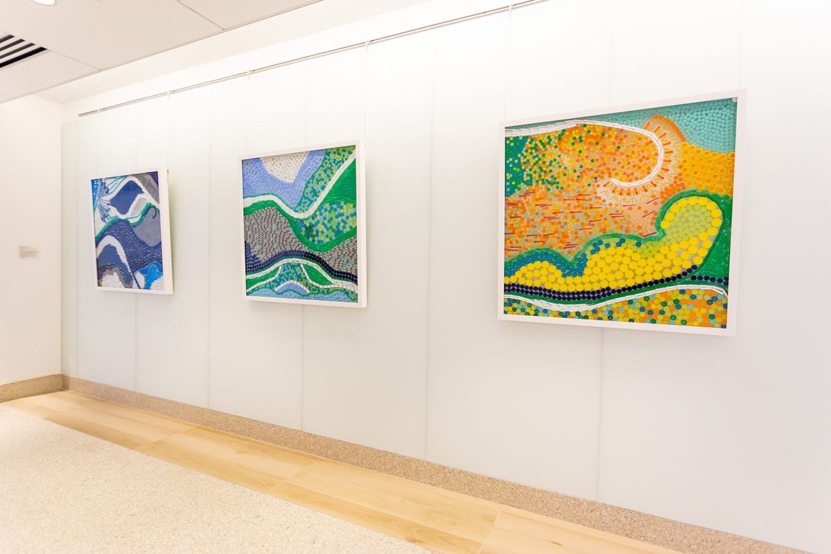 Photograph of Billie Coursey-Lookingbill's tryptic painting series, Water, Earth, Sun. Each painting has colors coordinating with the specific object, water - blue, earth - greens and blues, sun - yellows, oranges and greens. 