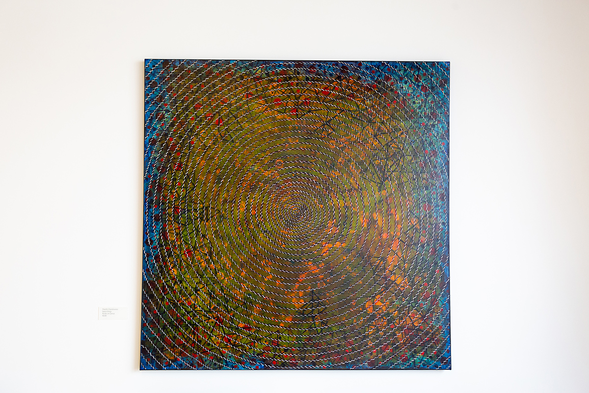 Photograph of Space Energy by Shanthi Chandrasekar, shown are white and black patterned lines spiraling from the middle overtop a centralized forest scene in the middle and blue sky surrounding the outer edges of the canvas.