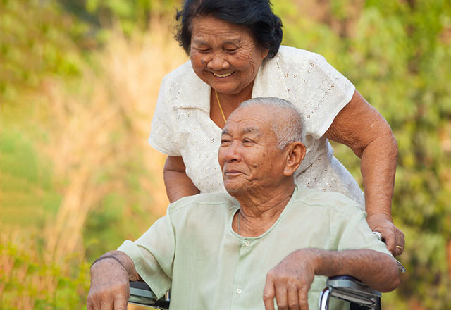 An older woman pushing her husband in a wheelchair