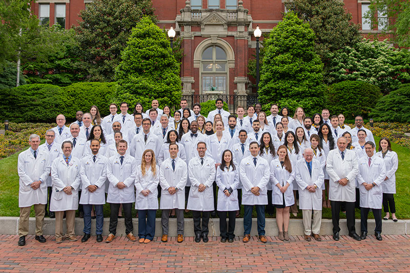 Group of residents in white coats standing together in front of the old brick entrance to the hospital.