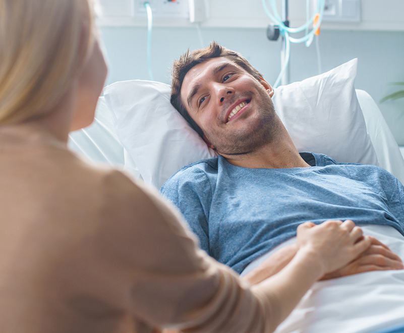 man smiling in hospital bed at loved one