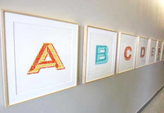 Photo showing the artwork displayed in a hallway, listing letters designed and colored.