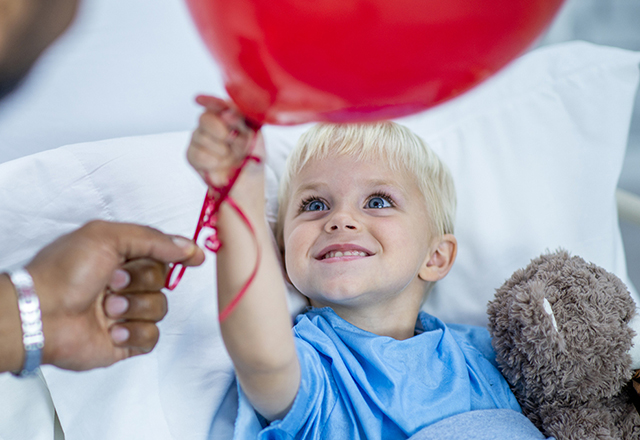 boy in hospital bed holding red balloon