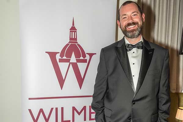 Thomas V. Johnson in a tuxedo, posing in from of a sign that reads Wilmer