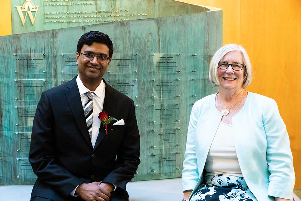 Pradeep and Sheila seated together in front of a glass wall