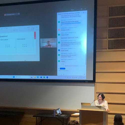 Heather Connors presents at a lectern with a large projection screen behind her