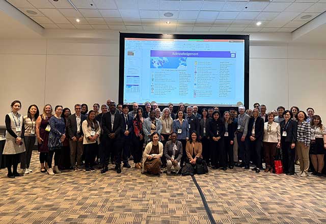 Large group of scholars standing in front of a presentation screen