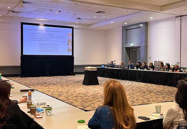 A large panel sits around a U shaped table with a large presentation screen in the middle