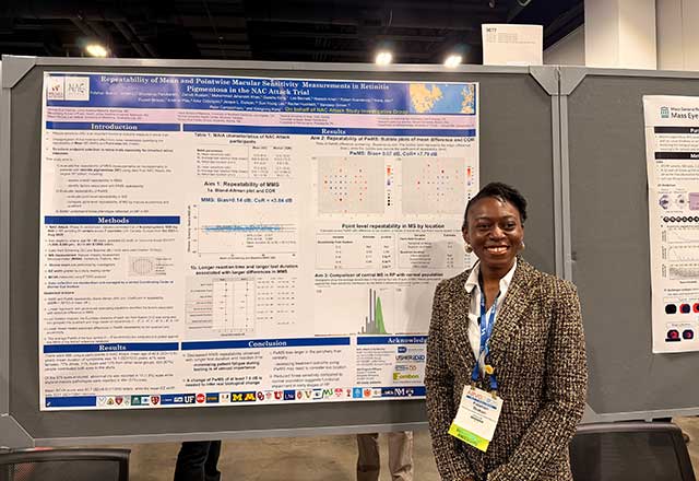 Researcher smiles in front a research poster