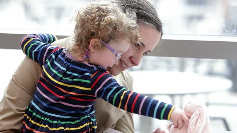 Woman holds a young girl, who reaches toward a stuffed bunny toy