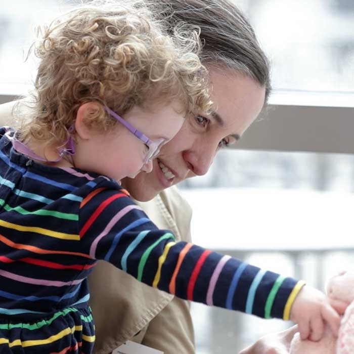 Woman holds a young girl, who reaches toward a stuffed bunny toy