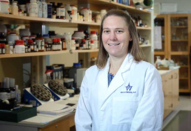 Malia Edwards in a white coat standing in her lab