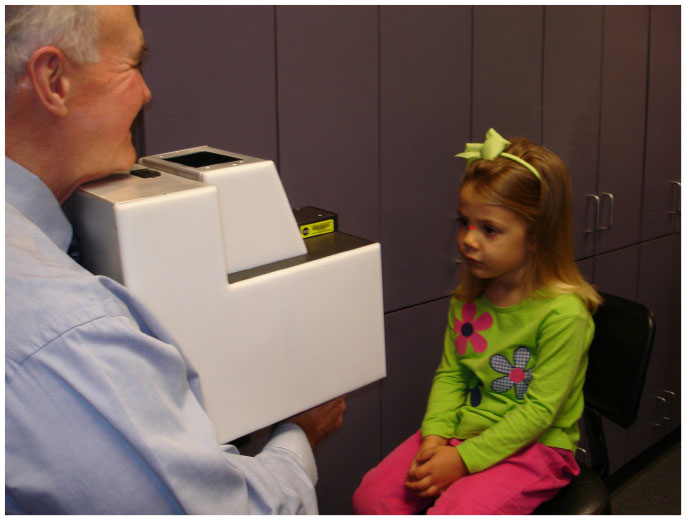 Doctor Guyton examines a young patient, who gazes into a device he holds. 