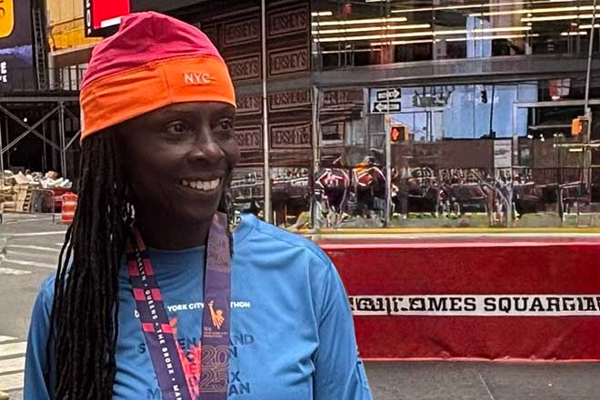 Jackie in a bright orange and red hat, smiling in front of a busy New York cityscape