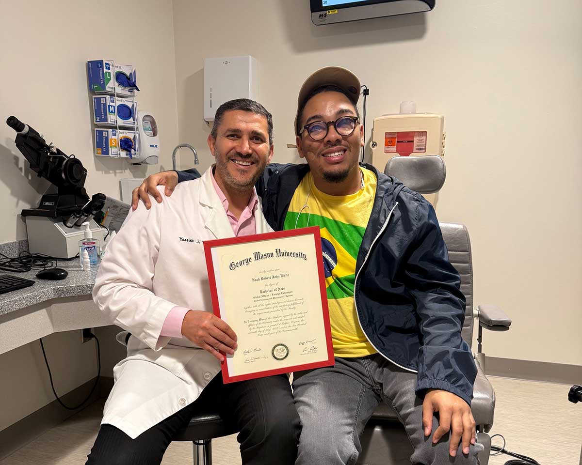 Doctor Daoud and Noah White smiling together in an exam room. Doctor Daoud holds Noahs George Mason University diploma