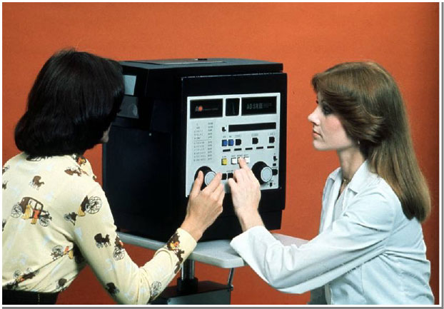 Two women adjust the knobs on a machine from the 70s