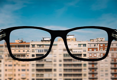 Glasses held up against buildings on the horizon to illustrate myopia, a common refractive error