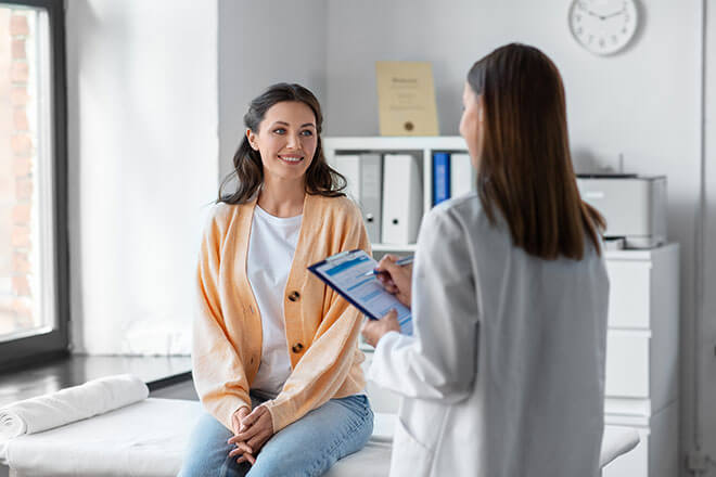 A woman sits in the clinic office listening to her doctor