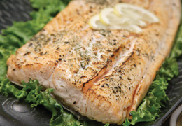 Seasoned salmon on a plate with lemon wedges on a bed of lettuce.