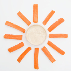 Small bowl of hummus surrounded by carrot sticks spread around it like rays of sunshine.