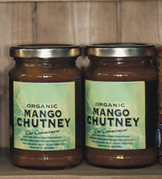 Two jars of mango chutney sitting on a shelf.