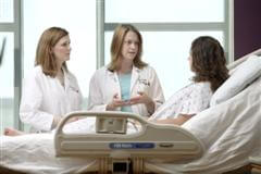 two medical professionals speaking with a patient in a hospital bed