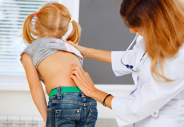 a pediatrician checks a young girl for scoliosis