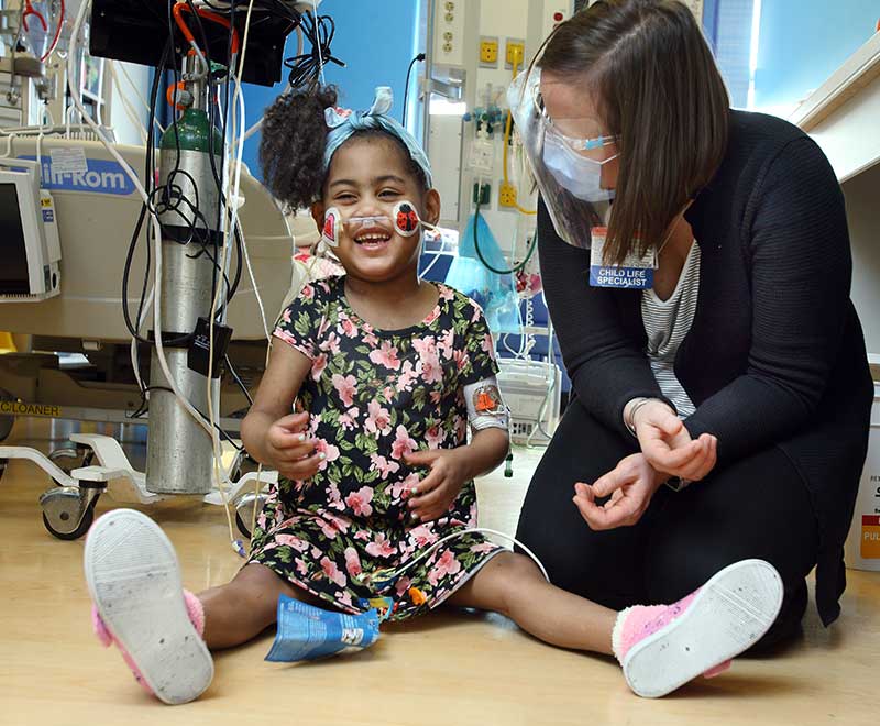 A child life specialist and young girl sit on the floor