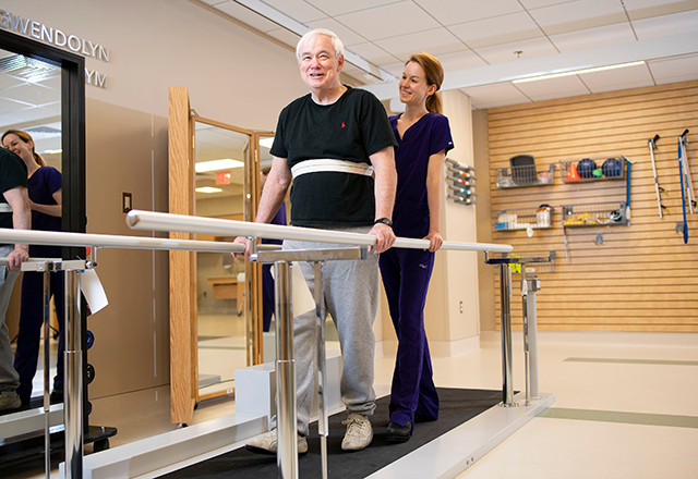a physical therapist helping a patient walk with the help of support bars