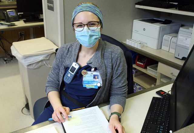 Amy Penney sits at a desk, wearing a mask.