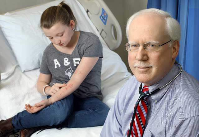 Dr. Robert Wood in a hospital room with his pediatric allergy patient as she looks at the allergy test on her arm