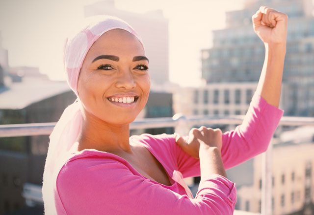 Woman dressed in pink, smiling with a strong arm up. 
