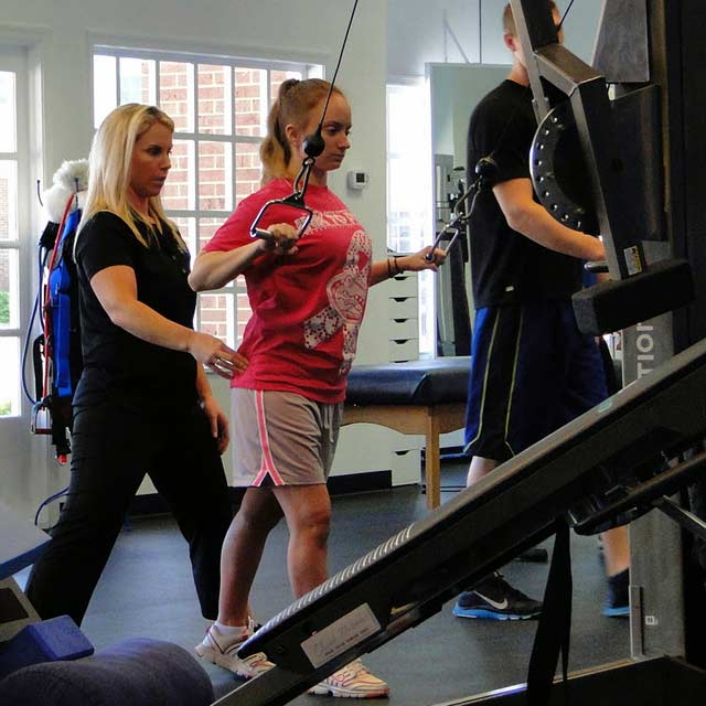 A woman exercising in the gym with help from a health care professional