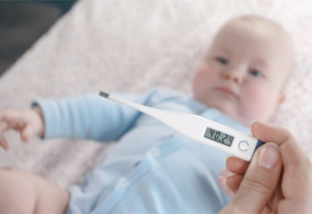 A parent holds a thermometer above a baby, who lays on a blanket.