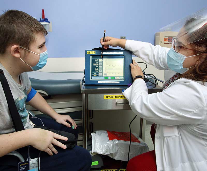 A nurse and a teenage boy look at a monitor together