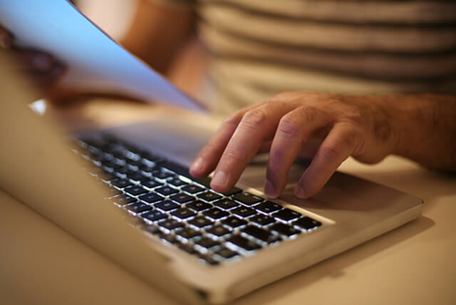Person holding paper in one hand while typing on laptop.