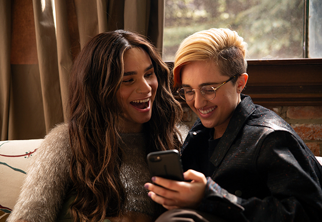 A transfeminine non-binary person and transmasculine gender non-conforming person looking at a phone and laughing