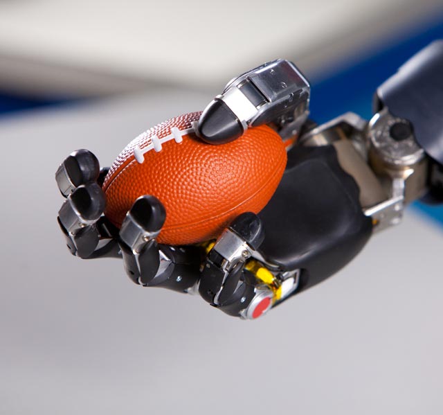 A photo shows a prosthetic hand picking up a ball. 